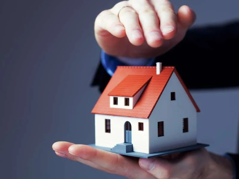 Hands protecting a house model symbolizing insurance coverage