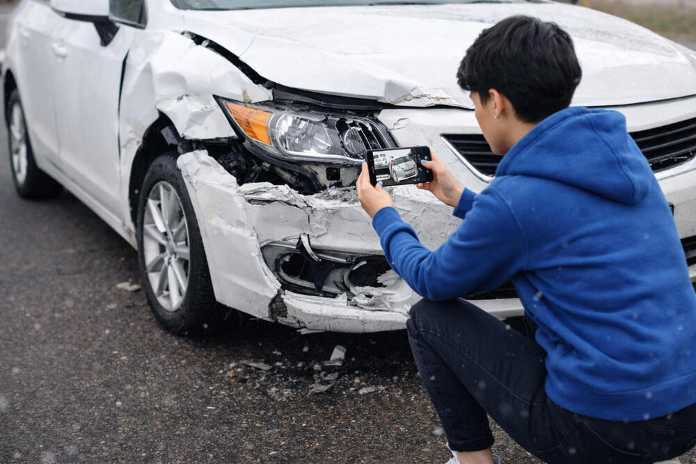 Driver photographing vehicle damage after a car accident before filing an insurance claim