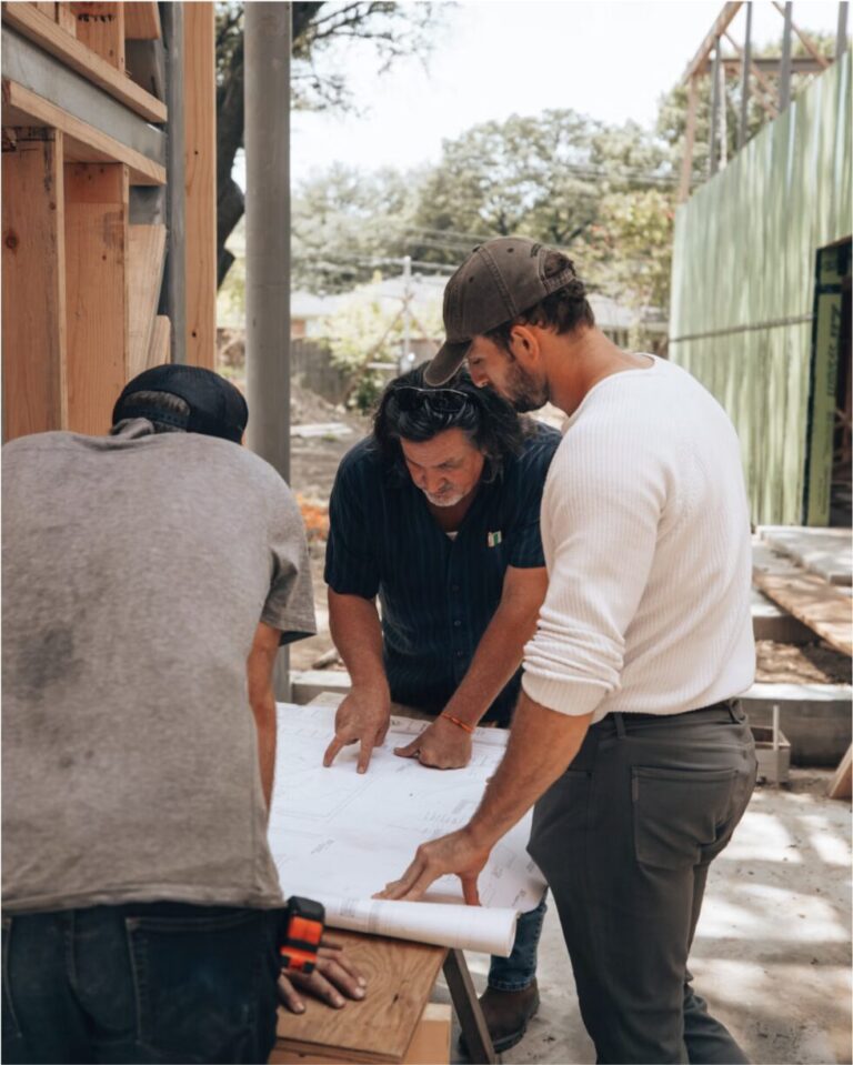 Three professionals reviewing blueprints together at a residential construction site, representing a developer evaluating insurance decisions before buying.